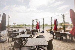 Een terras buiten met tafels en stoelen, parasols en plantenpotten.