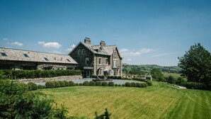 A large stone house with a well-manicured lawn, a circular driveway, and a view of rolling hills in the background. - 1 Bed in Windermere (oc-lr229) (Windermere)