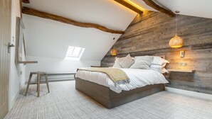 A bedroom with a sloped ceiling, exposed wooden beams, a bed with white linens, two pendant lights, and a small stool. - 1 Bed in Windermere (oc-lr229) (Windermere)