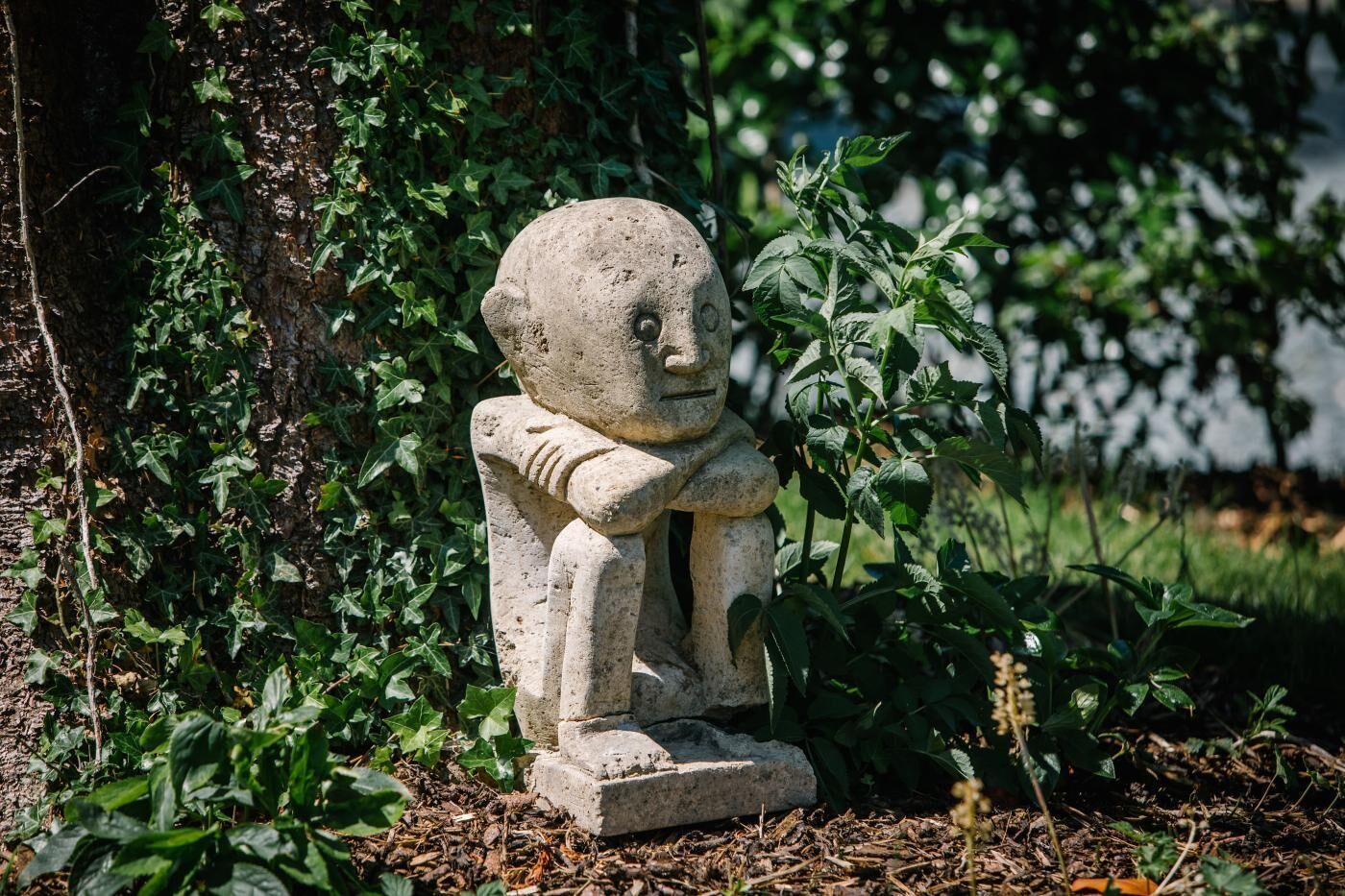 Eine steinerne Statue einer sitzenden Figur in einem Garten.