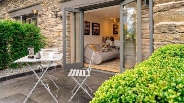 A stone building with a patio area, a dining table, and a sofa. - 1 Bed in Windermere (oc-lr229) (Windermere)