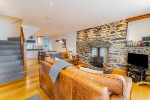 A living room with a stone fireplace, leather sofa, and a TV. - 3 Bed in Ambleside (oc-lr021) (Ambleside)