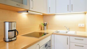 A modern kitchen with white cabinets, a stainless steel coffee maker, a sink, and a built-in oven. - Ferienwohnung mit Balkon und Freizeitangeboten in Sellin (Sellin)