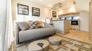 Una sala de estar moderna con sofá, reposapiés y una cocina al fondo.