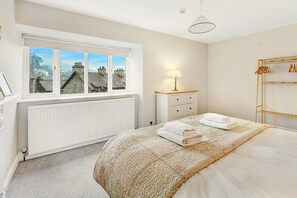 A bedroom with a large window, a radiator, a bedside table with a lamp, a bed with a textured blanket, and a wooden wardrobe. - 3 Bed in Ambleside (oc-lr012) (Ambleside)