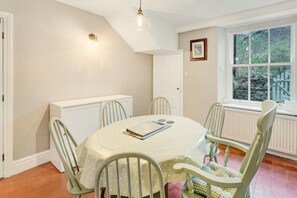 A dining room with a round table, four chairs, a radiator, a window with a view of greenery, and a light fixture. - 3 Bed in Ambleside (oc-lr012) (Ambleside)