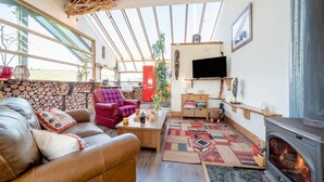 Un salon chaleureux avec une cheminée, un canapé en cuir, un fauteuil rouge et un téléviseur fixé au mur.