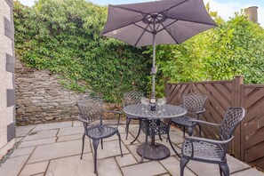 An outdoor patio with a round table and four chairs, a large umbrella, and a stone wall. - 2 Bed in Windermere (oc-lr001) (Windermere)