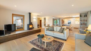 Ein modernes Wohnzimmer mit Sofa, Couchtisch, Fernseher, Kamin und Blick in die Küche.