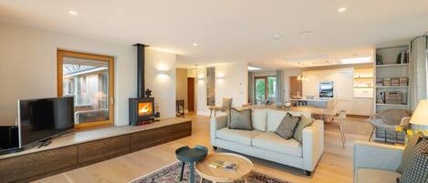 A modern living room with a sofa, coffee table, TV, fireplace, and a view into the kitchen.