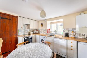 A compact kitchen with a dining table, a washing machine, and a built-in oven. - 3 Bed in Hawkshead (oc-lr238) (Hawkshead Hill)