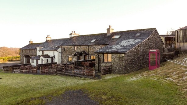 A stone building with a sloped roof, a small porch, and a red telephone booth. - 3 Bed in Hawkshead (oc-lr238) (Hawkshead Hill)