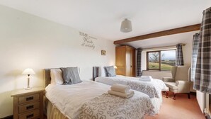 A bedroom with two beds, a wooden wardrobe, a chair, and a window with a view. - 3 Bed in Hawkshead (oc-lr238) (Hawkshead Hill)