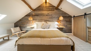 A bedroom with a sloped ceiling, wooden beams, a bed with pillows, a chair, a bedside table, and a wardrobe. - 1 Bed in Windermere (oc-lr232) (Windermere)