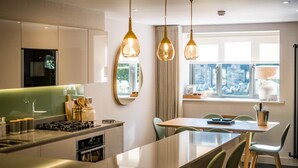 A modern kitchen with a central island, pendant lighting, and a dining area with a view of the city. - 3 Bed in Windermere (oc-lr235) (Windermere)
