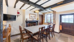 Ein Essbereich mit Tisch und Stühlen, einem Kamin, einem an der Wand montierten Fernseher und einem Fenster mit Vorhängen.