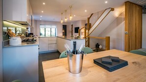 A modern kitchen with a central island, a dining area with a wooden table, and a staircase leading to an upper level. - 3 Bed in Windermere (oc-lr228) (Windermere)