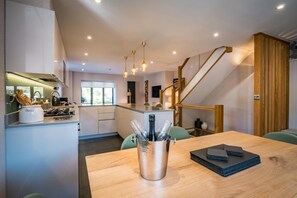 A modern kitchen with a central island, a dining area with a wooden table, and a staircase leading to an upper level. - 3 Bed in Windermere (oc-lr228) (Windermere)