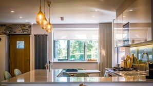 A modern kitchen with a central island, pendant lighting, and a view of greenery outside. - 3 Bed in Windermere (oc-lr228) (Windermere)