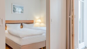 A hotel room with a bed, a nightstand, a lamp, a framed picture on the wall, and a window. - Ferienwohnung Seepark Sellin mit Ahoi Badewelt & Balkon (Sellin)