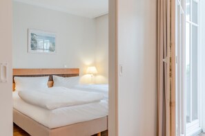 A hotel room with a bed, a nightstand, a lamp, a framed picture on the wall, and a window. - Ferienwohnung Seepark Sellin mit Ahoi Badewelt & Balkon (Sellin)