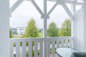 A covered outdoor area with a glass table, white railings, and a view of a building and trees. - Ferienwohnung Seepark Sellin mit Ahoi Badewelt & Balkon (Sellin)