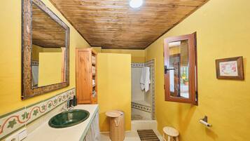 Un baño con techo de madera, un lavabo verde, un mueble de madera, un espejo y una ventana.