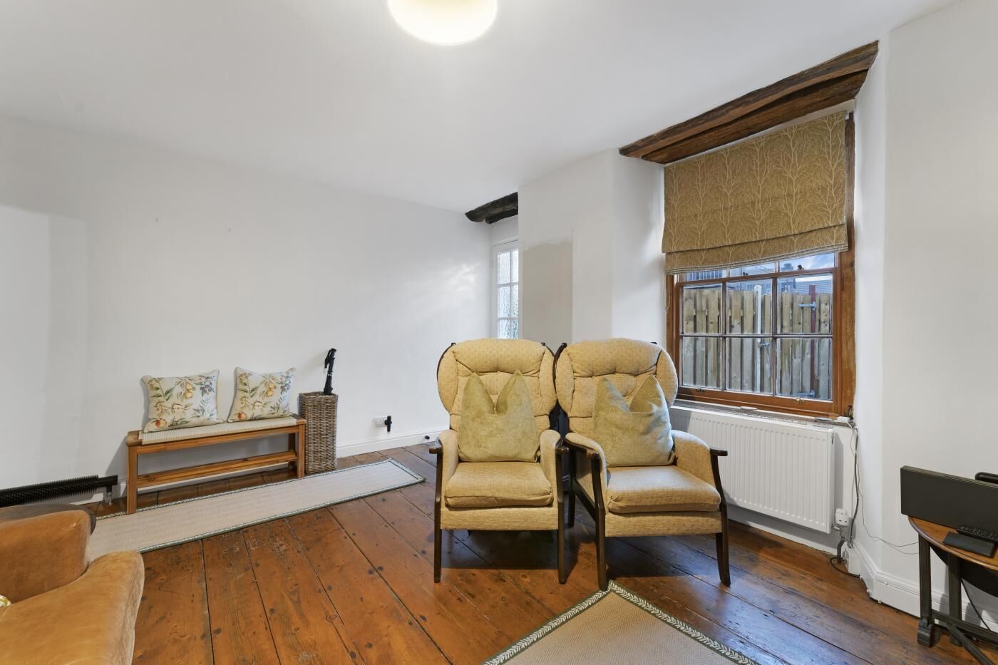 A room with a wooden floor, a large window with a view, a sofa, and a chair.
