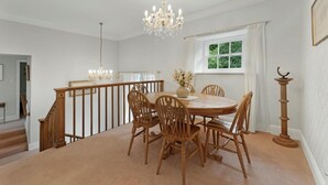 Een eetruimte met een ronde tafel, houten stoelen, een kroonluchter en een raam met gordijnen.