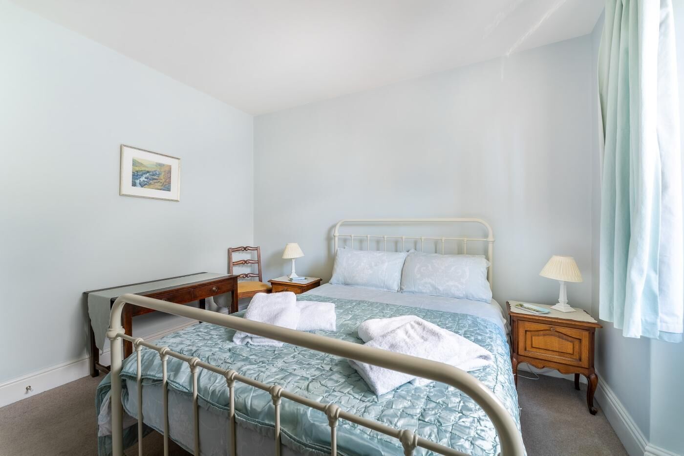 Quarto com estrutura de cama de metal, mesa de cabeceira de madeira e uma cama simples com colcha estampada azul.