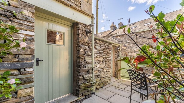 A stone house with a green door, a small window, and a patio with outdoor furniture. - 3 Bed in Ambleside (oc-lr030) (Ambleside)
