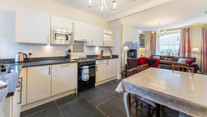 A modern kitchen with white cabinets, a gas stove, a microwave, and a dining area with a table and chairs. - 3 Bed in Ambleside (oc-lr030) (Ambleside)