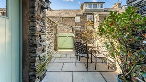 A stone-walled courtyard with a green gate, outdoor seating, and a potted plant. - 3 Bed in Ambleside (oc-lr030) (Ambleside)