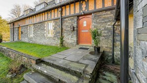 Una casa in pietra con una porta in legno, un piccolo giardino antistante e una scala in pietra che conduce all'ingresso.