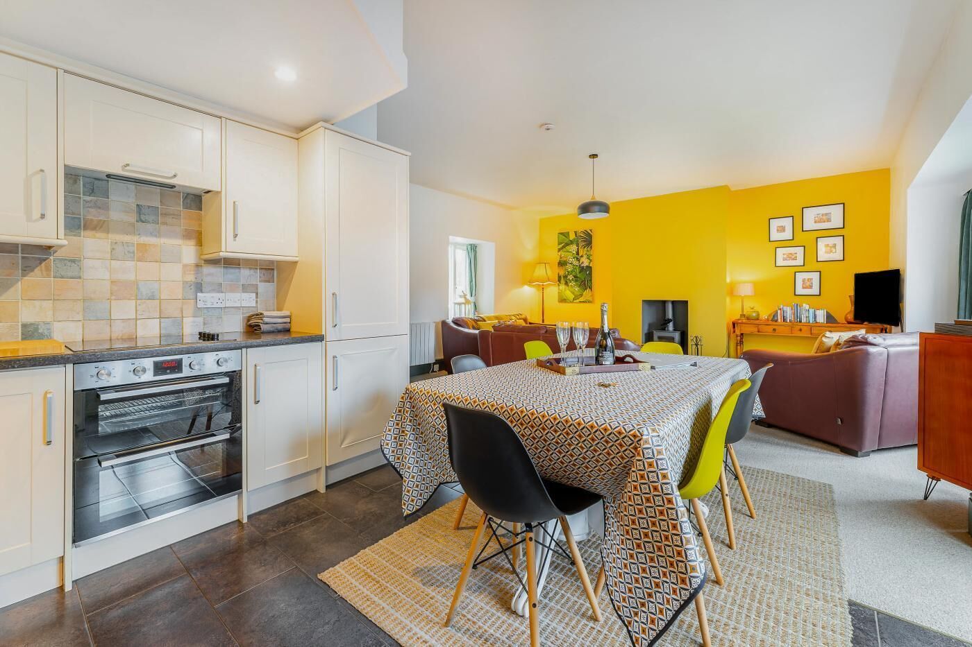 A modern kitchen with white cabinets, an oven, and a dining area with a patterned tablecloth.