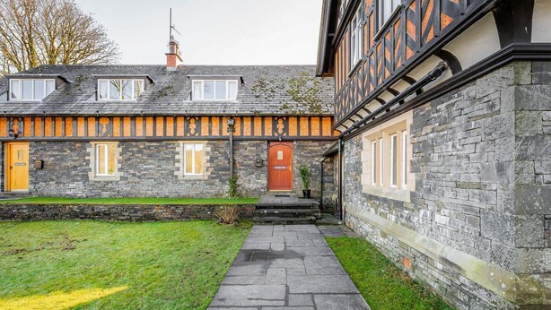 Un edificio in pietra con una porta di legno, un vialetto in pietra e una zona verde.
