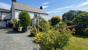 A two-story house with a gravel driveway, a conservatory, and a garden with various plants and flowers. - 3 Bed in Chapel Stile (oc-lr202) (Chapel Stile)