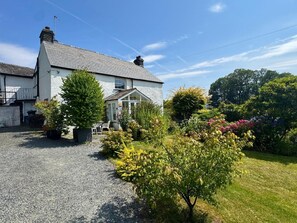 A two-story house with a gravel driveway, a conservatory, and a garden with various plants and flowers. - 3 Bed in Chapel Stile (oc-lr202) (Chapel Stile)