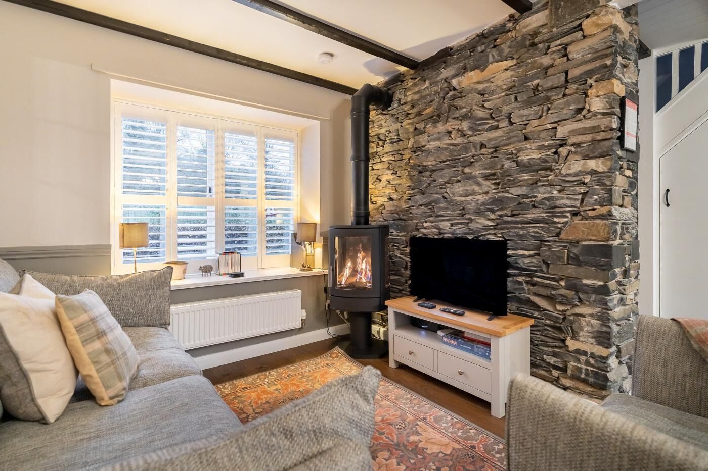A cozy living room with a stone wall, a fireplace, a sofa, and a television.