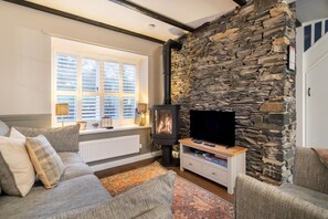 Ett mysigt vardagsrum med en stenmur, en öppen spis, en soffa och en tv.