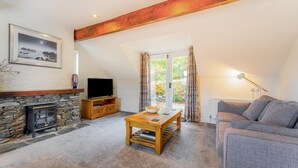 A cozy living room with a stone fireplace, a television, a wooden coffee table, and a sofa. - 2 Bed in Ambleside (oc-lr041) (Ambleside)