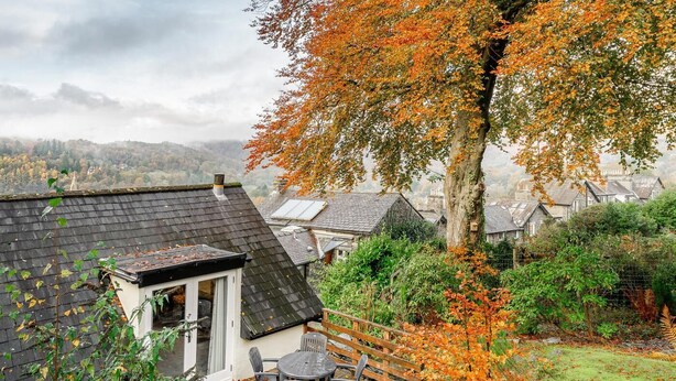 A residential area with houses, a tree with autumn leaves, and a small patio with outdoor furniture. - 2 Bed in Ambleside (oc-lr041) (Ambleside)
