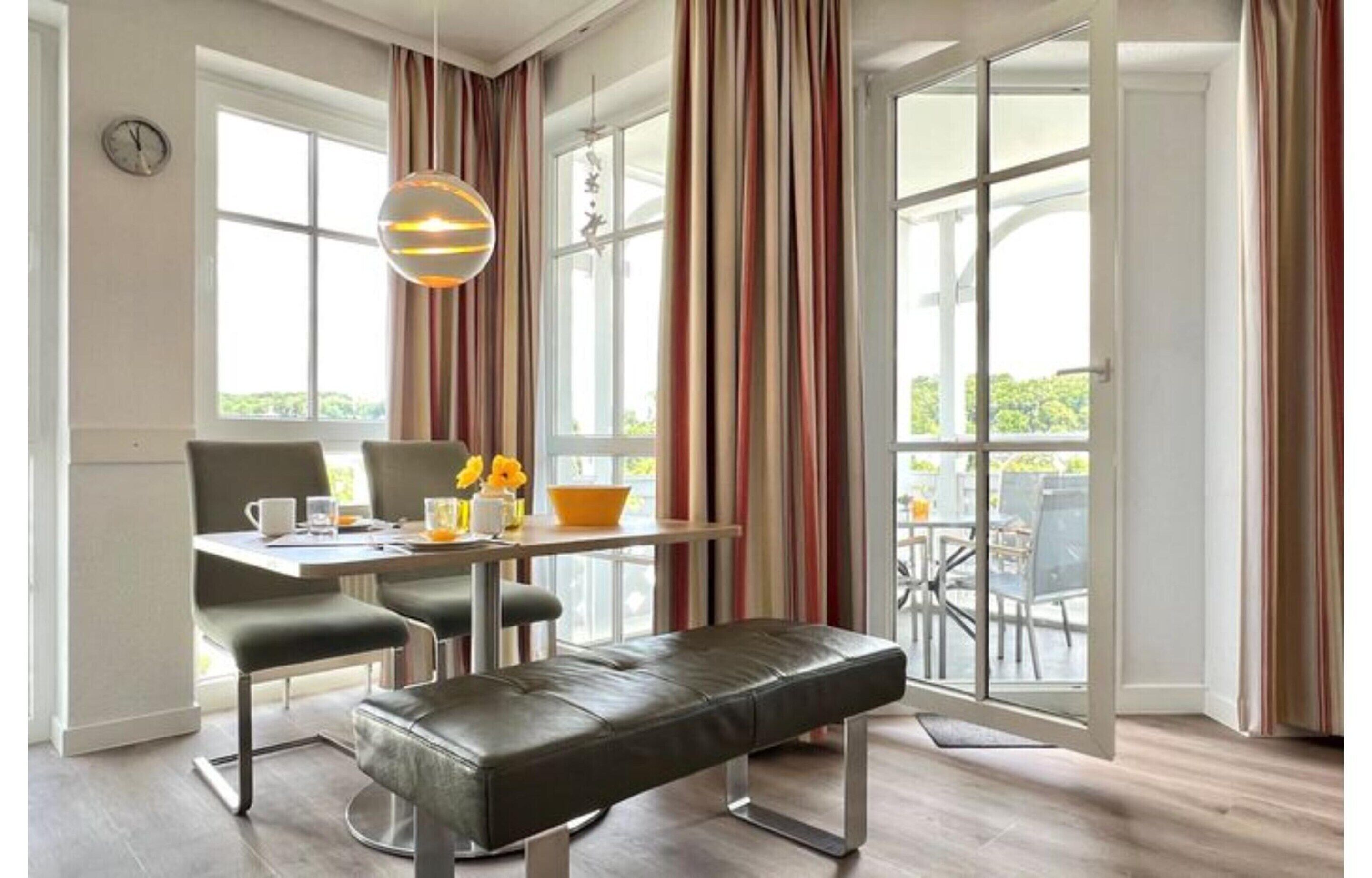 A modern dining area with a table, chairs, and a bench. There is a window with curtains, a hanging light fixture, and a view of the outdoors.