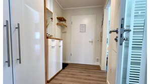 Um corredor com piso de madeira, paredes brancas, uma porta com uma pequena placa e uma porta branca com maçaneta.
