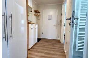 Ein Flur mit Holzboden, weißen Wänden, einer Tür mit kleinem Schild und einer weißen Tür mit Griff.