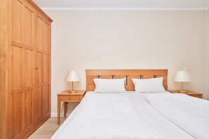 A bedroom with a large wooden wardrobe, two bedside tables with lamps, and a bed with white bedding. - Helle und Gemutliche Ferienwohnung mit Balkon in Sellin (Sellin)