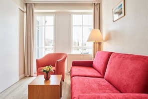 A room with a red sofa, a wooden coffee table with a vase, a pink armchair, and a window with curtains. - Helle und Gemutliche Ferienwohnung mit Balkon in Sellin (Sellin)