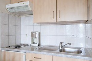 A kitchen with a built-in stove, a coffee maker, a sink, and wooden cabinets. - Helle und Gemutliche Ferienwohnung mit Balkon in Sellin (Sellin)