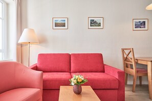 A red sofa, a wooden coffee table with a vase, a wooden chair, and a lamp. - Helle und Gemutliche Ferienwohnung mit Balkon in Sellin (Sellin)