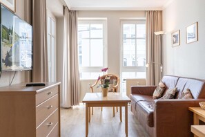 Ein Wohnzimmer mit einer Couch, einem Tisch mit Topfpflanze, einem Fernseher und einem Fenster mit Vorhängen.